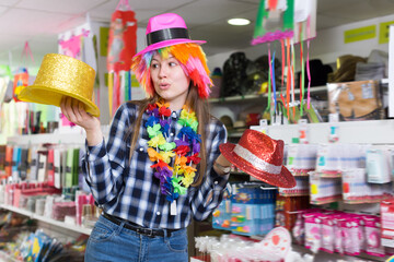 Young woman preparing for party, choosing funny headdresses in store