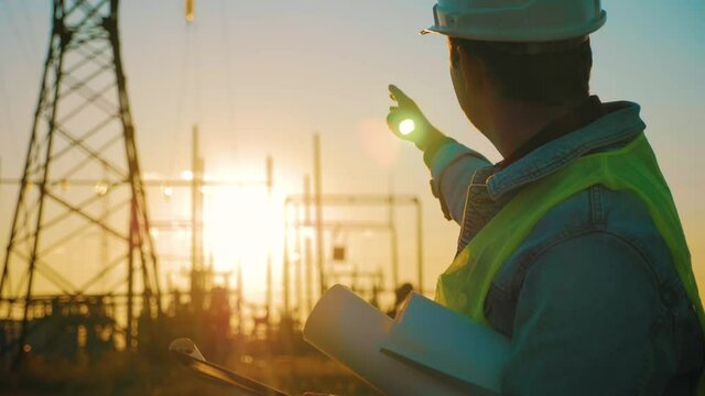 Industry energy business concept. Silhouette electrical engineer a working near tower with electricity at sunset time. Electrical worker inspect voltage electricity pylon. Power generation industry.