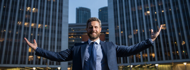 Businessman raising arms near cityscape office building. Happy, success and business triumph, celebrating victory. - obrazy, fototapety, plakaty