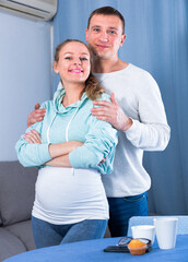 Smiling middle-aged couple expecting child and spending time at home