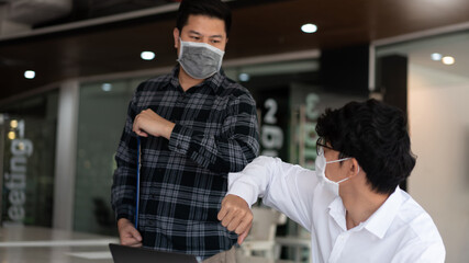 Covid-19 concept Coronavirus two male colleagues wearing protective face masks greeting bumping elbows at office protecting from Coronavirus outbreak (COVID-19)