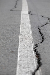Cracks in the asphalt in the city park. Bicycle path with a white dividing strip. 