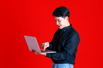 Asian young man standing look at camera and smile feel confident.Hold laptop on hand.Shoot in studio with red background with copy space use to be design advertising banner in concept tutor learning