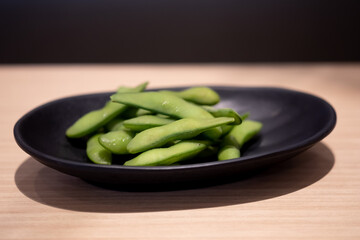 Boiled Edamame, green soybeans on black dish.