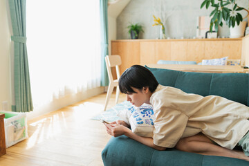 ソファに寝そべりスマートフォンを見る女性