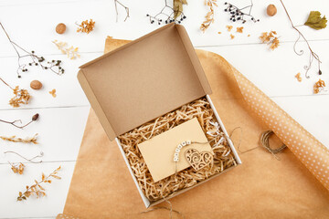 Eco friendly packaging of a gift box in a paper wrap. Top view on white wooden background Decorated by Autumn leaves. Donation. Zero waste. Autumn present. Craft present box. Fall party celebration. 