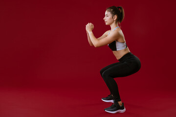 young caucasian woman in sports black clothing exercising by fitness on a red background. Healthy lifestyle concept