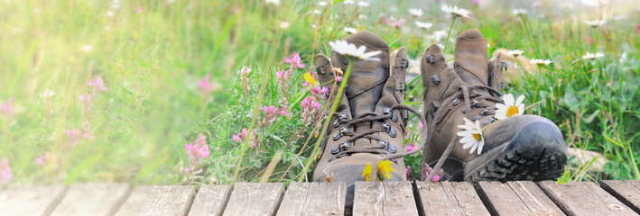 old hiking shoes in a meadow with flowers bloming and a wooden terrace