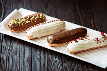 French dessert eclairs or profiteroles with chocolate glaze, with different toppings on a white...