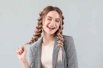 Beautiful young woman with braided hair on grey background - obrazy, fototapety, plakaty