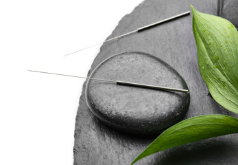 Acupuncture needles and spa stone on white background