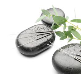 Acupuncture needles and spa stones on white background