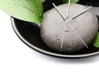 Bowl with acupuncture needles and spa stone on white background, closeup