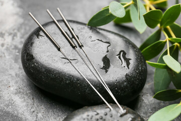 Acupuncture needles and spa stone on grey background