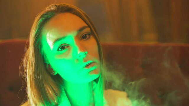 A girl smokes a hookah in a nightclub with a green light