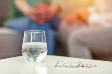 Cropped shot of two unrecognizable women sitting on the sofa with a pillbox and water in the living...