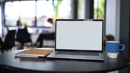 Mock up laptop computer, notebook and coffee cup on black wooden table in office.
