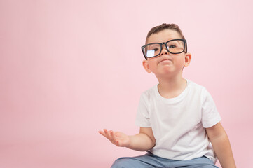 Portrait of a little boy in glasses, dressed in white t-shirt, pink background with copy space