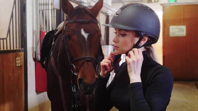 Equestrian - a woman in black clothes putting on a black plastic helmet