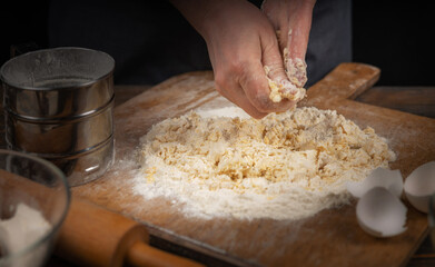 Women's hands, flour and dough. A woman in an apron prepares dough for homemade baking, a rustic home cozy atmosphere, a dark background with unusual lighting.