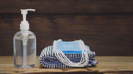 Clear hand sanitizer bottle Placed close to the black and white striped towels There is a mask on the cloth. On the brown plank floor, copy space concept covid-19, sterilized.