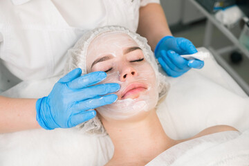 Obraz na płótnie Canvas Treatment, cure of face skin in cosmetology clinic. Beauty procedure with problem skin for young woman. Cosmetologist doctor is applying cream with anesthesia before PRP therapy procedure.