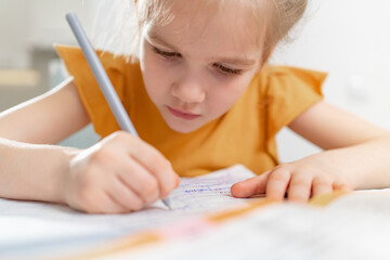 A concentrated little schoolgirl does her homework. complexities of correct and beautiful handwriting. there is no desire to learn. family and distance learning. selective focus. 