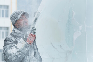 The sculptor cuts a figure from an ice block with a gasoline saw