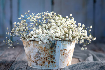 Blumenstrauß aus der weißen Schleierkraut steht in der antik Metallvase auf dem alten Holz, dekoriert mit dem Graustoff. Hintergrund ist hellblau, alte Holztür. Vintage,  hellblau, grau. Querformat