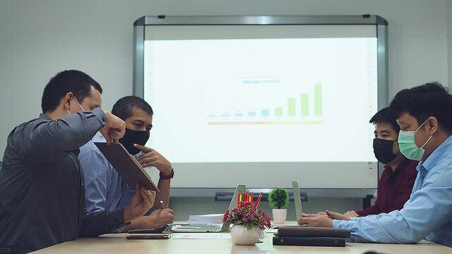 Businessmen wearing protective masks discussing and work together in meeting room. Social distance practice prevent coronavirus COVID-19.