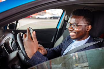 Distracted driving can increase the chance of a road accident. Portrait of a happy man texting and driving in his car on his cell phone. Businessman using mobile phone in the car