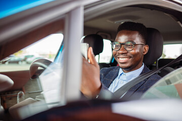 Distracted driving can increase the chance of a road accident. Portrait of a happy man texting and driving in his car on his cell phone. Businessman using mobile phone in the car