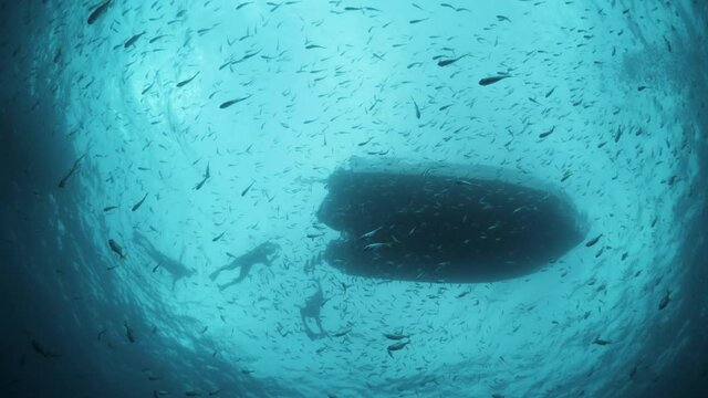 Unique underwater photography perspective Snell's window of a large boat with snorkelers swimming and floating in the clear blue water with masses of schooling fish.