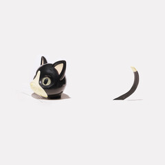 Minimal concept. Only a toy cat head and its tail above white surface. Side angle.