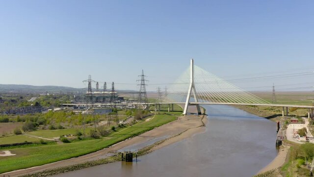 Flint bridge drone jib up shot. Sunny UK summers day showing bridge and power station next to river Dee. 

Modern looking road bridge over the river Dee.