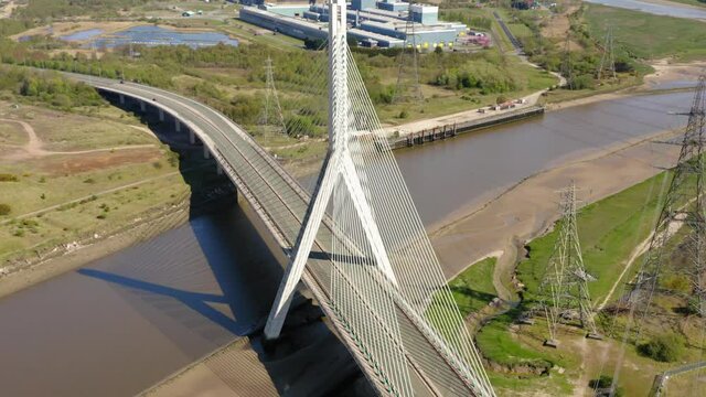 Modern suspension road bridge in Flint Wales with single white road car passing under. Drone shot with cinematic tilt down and rotation.