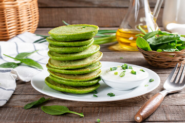 Green spinach pancakes with sour cream on a wooden table. Healthy food, diet