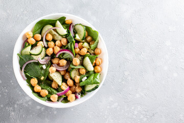 Chickpea salad with cucumber, spinach, parsley, onions and lemon in a plate on a served table. Tasty and healthy vegetarian food, oriental and Mediterranean cuisine. Top view. Copy space.