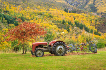 An old tractor in a field, with a hillside covered in bright autumn foliage behind. Photographed at...