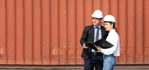 An officer from the Customs Department inspects the cargo in the container yard. Business man in hardhat helmet and caucasian woman foreman worker discuss togetherness