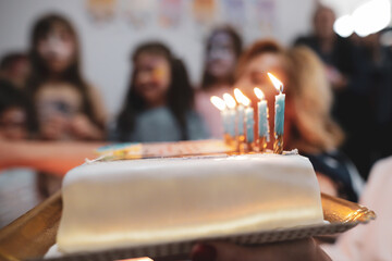 Shallow depth of field (selective focus) image with lit candles on a cake during a child birthday party.