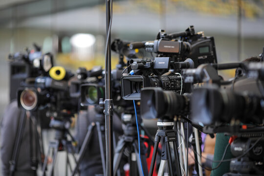 Shallow depth of field (selective focus) image with TV cameras on tripods on a press event.