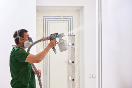 Worker painting wall with spray gun in white color.