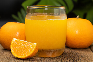 A glass of orange juice and orange fruit cut in half on the wooden table.