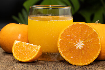 A glass of orange juice and orange fruit cut in half on the wooden table.