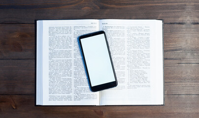 Open Bible book on a wooden table. Prayer. Phone on the book. Blank screen. Workplace in the office.