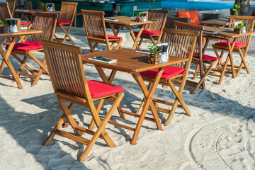 Fototapeta na wymiar Wooden table and chairs in empty beach cafe next to sea. Close up, Thailand