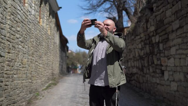 Caucasian male tourist 40 years old walks through the old city. He takes out his smartphone and takes pictures of the sights.