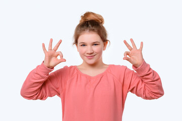 Portrait of a cute young girl in pink casual sweatshirt showing OK gesture with both hand. White background