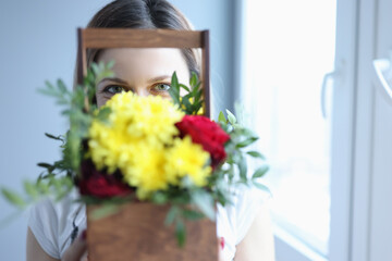 Woman holding wooden box with flowers in front of her face